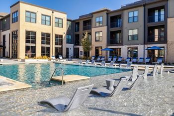 A pool with chairs and umbrellas in front of apartment buildings.